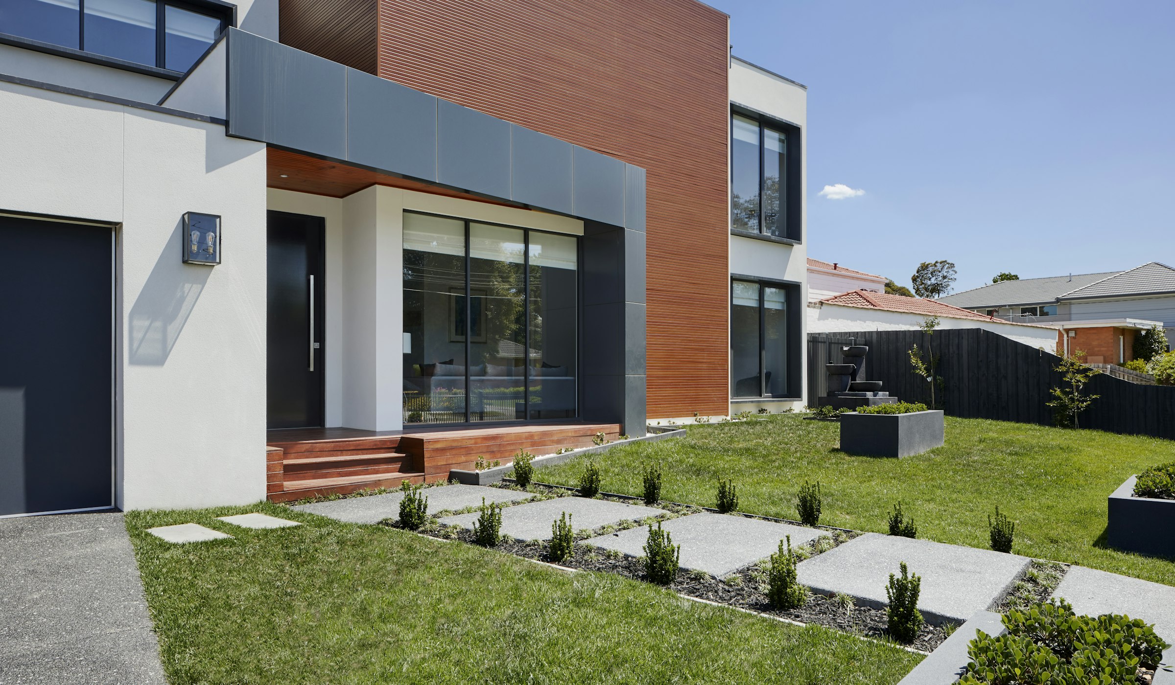 Wood-clad architecture with stepping-stone paving through a landscaped garden.