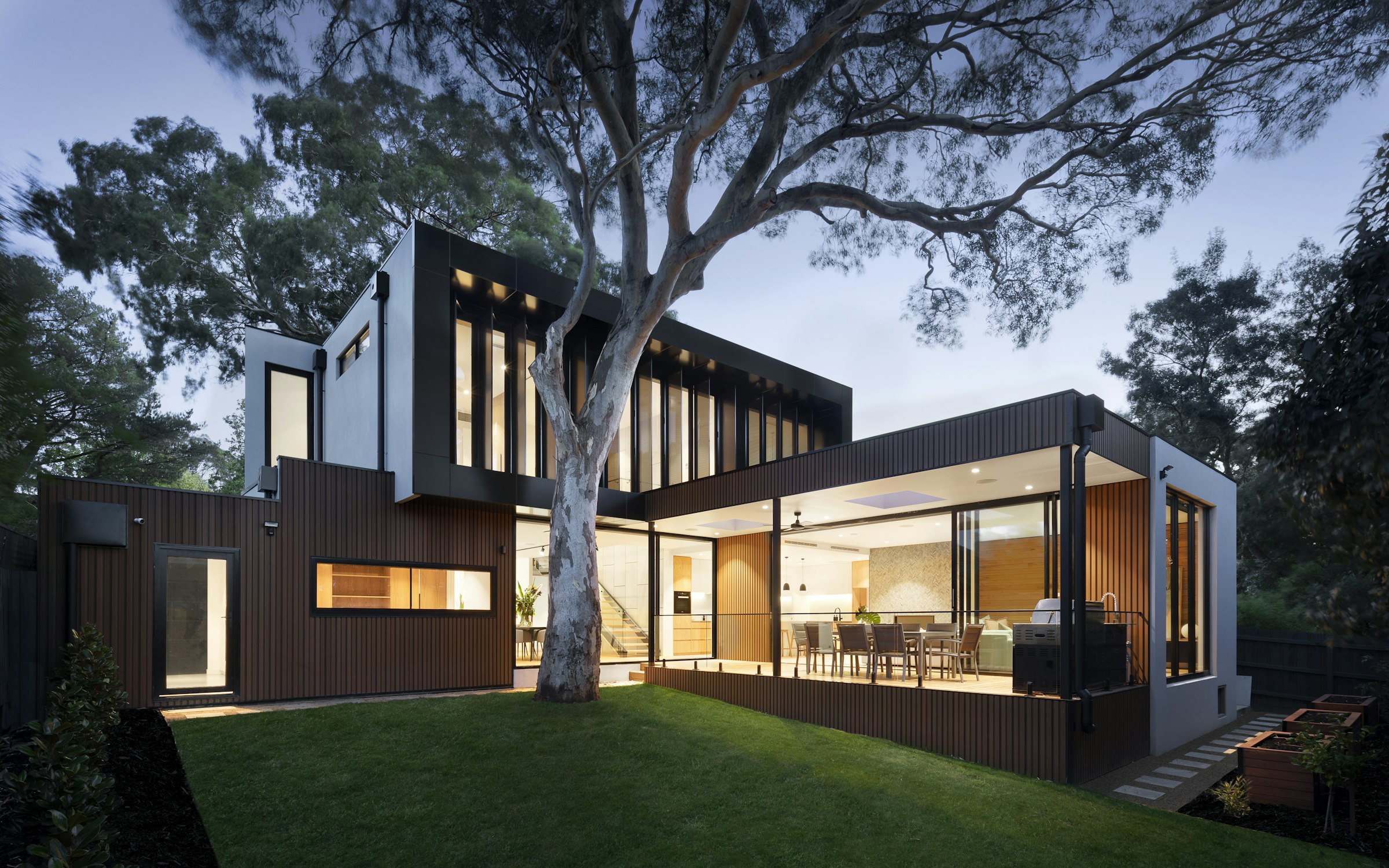 Contemporary residence at dusk with a mature tree rising through an open courtyard.