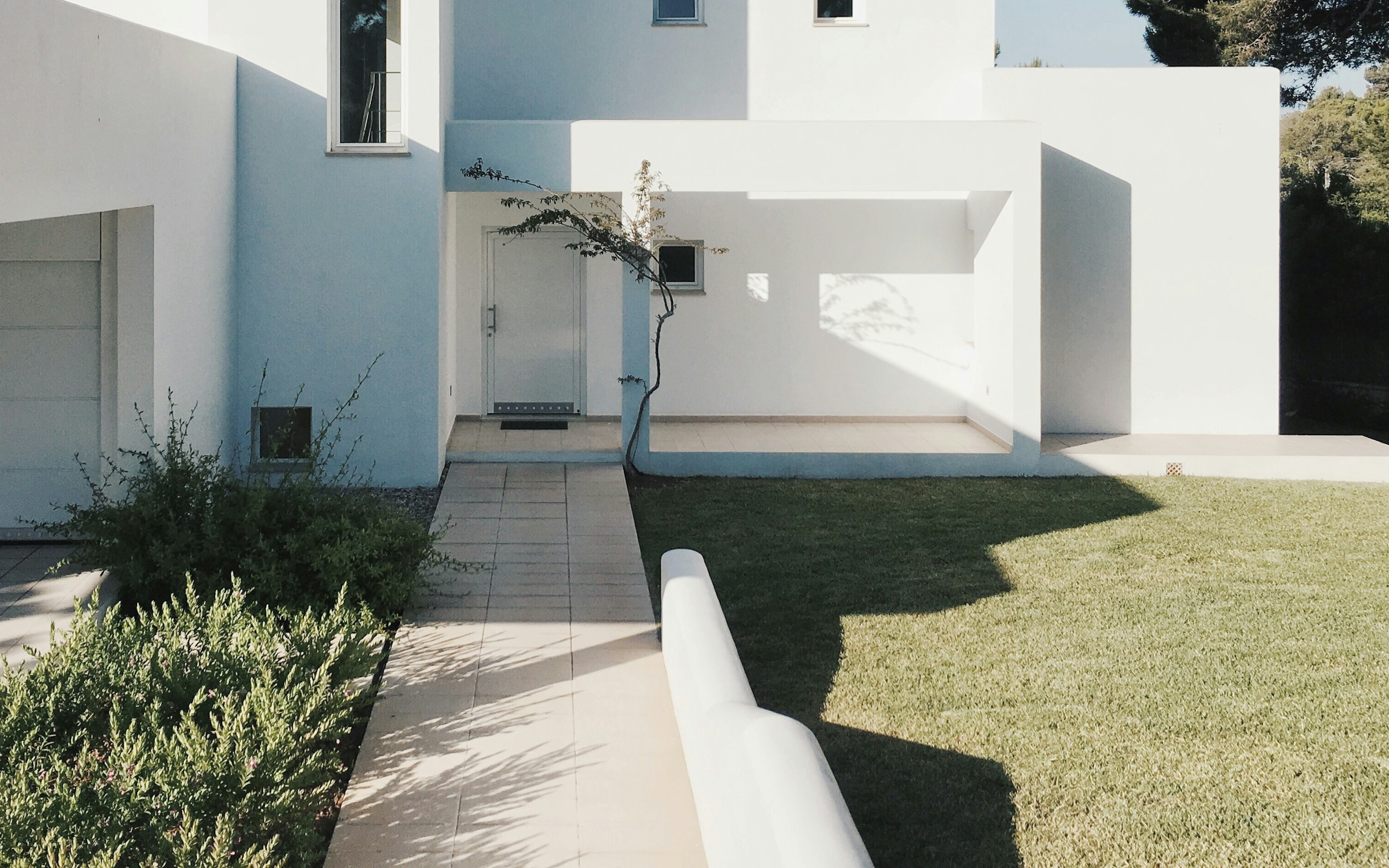 Minimalist white residence with a garden path leading to the entrance.